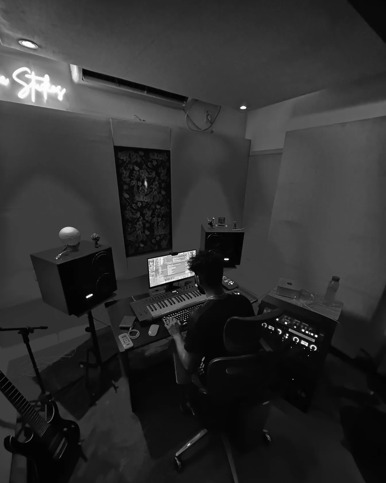 Rupendar at the desk in Mix Magic Studios, seen from above: two monitors on stands, a keyboard, the rack, and the neon sign on the wall.